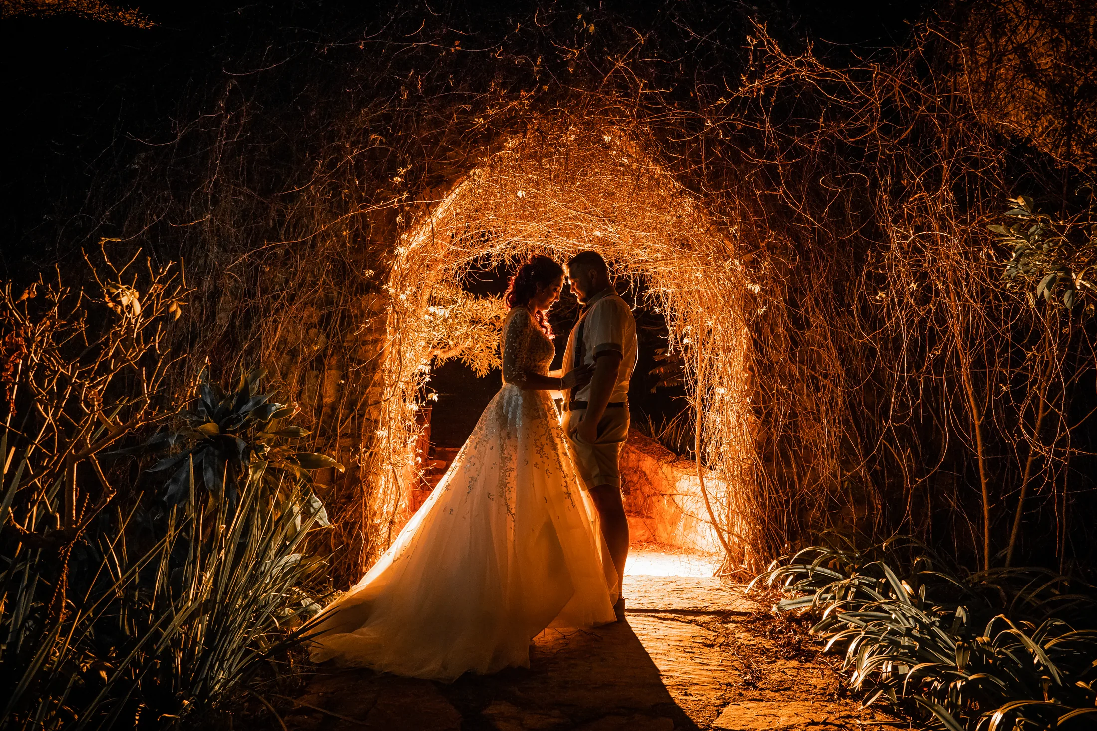 Armand and Melanie beneath an illuminated stone arch at night